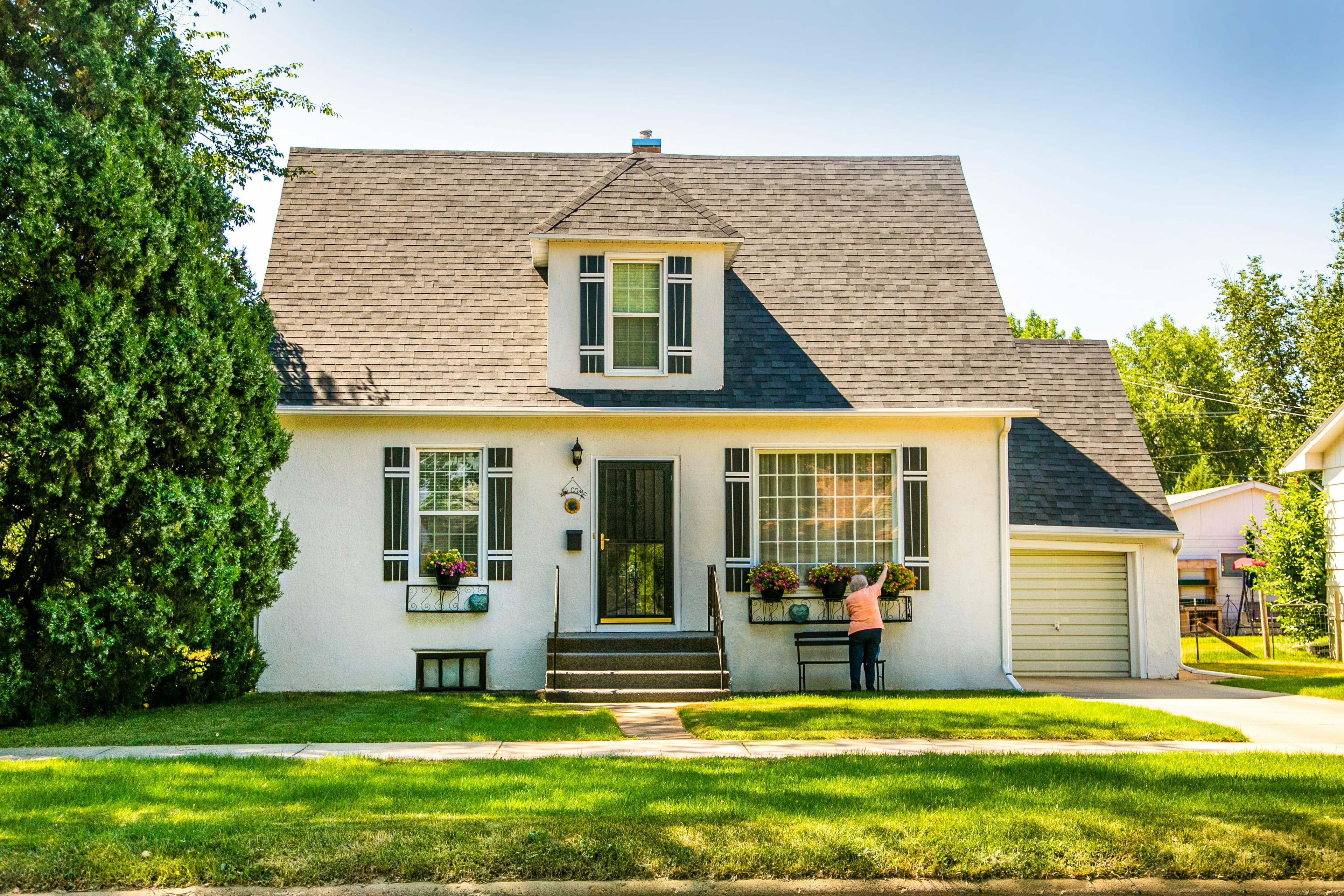 A house with a person standing in front, surrounded by greenery.