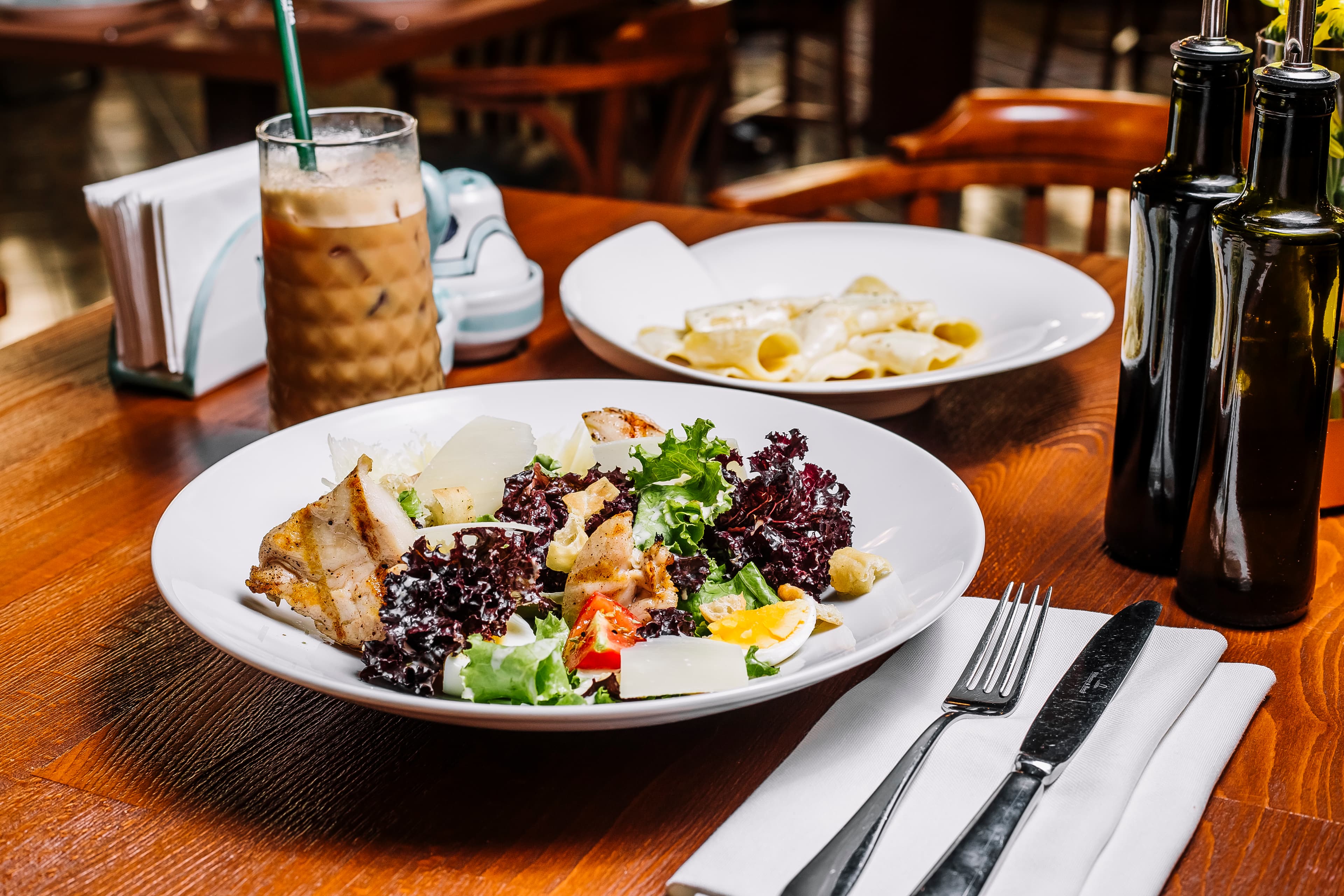 A beautifully arranged table featuring a fresh salad, a glass of wine, olive oil, and dining utensils for an elegant meal.